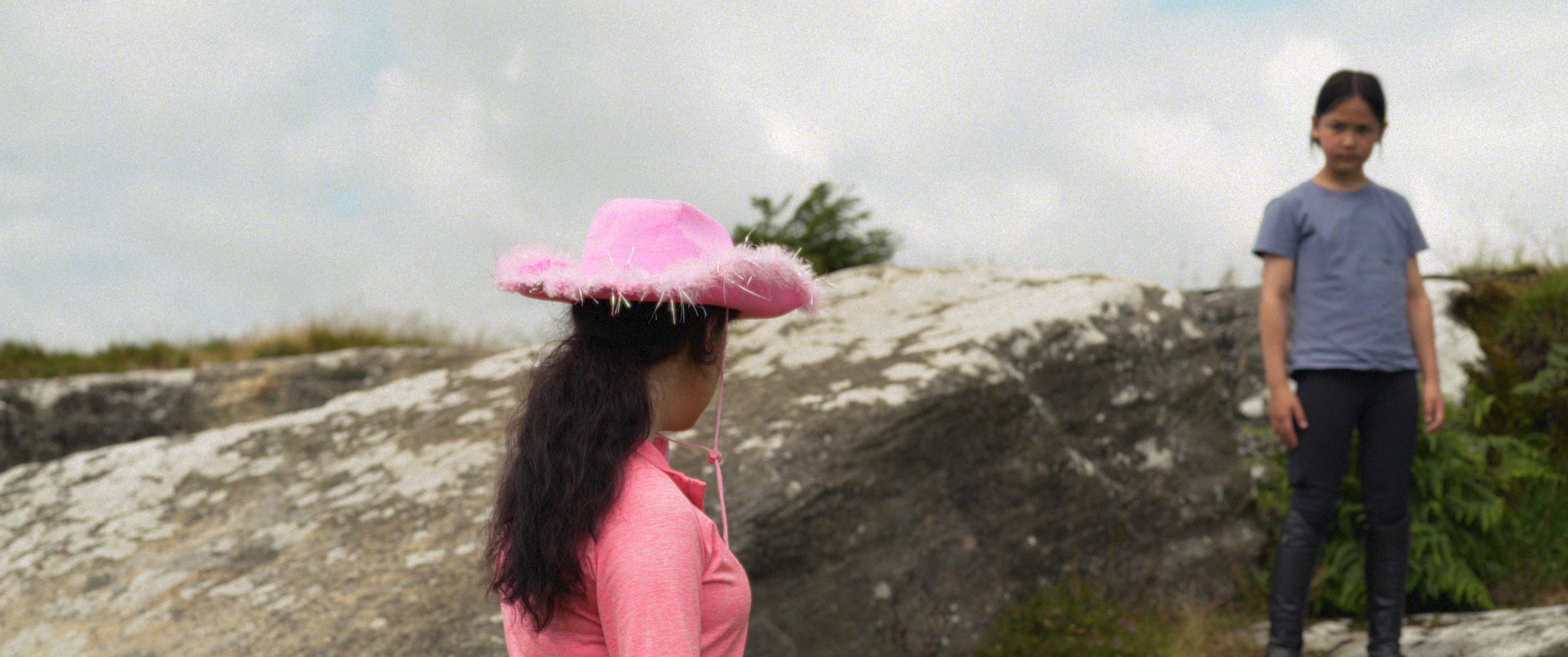 A girl wearing a pink cowboy hat looking over at her friend who is standing on a rock.